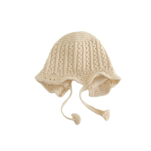 Cream knitted baby bonnet with ear flaps, lace-up straps and cable knit pattern