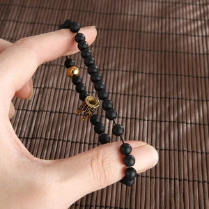 Detail eines Perlenarmbands mit schwarzen matten Perlen und goldenem Kronenanhänger
