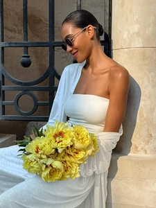 Close-up of white strapless top with knit shawl set against outdoor floral background