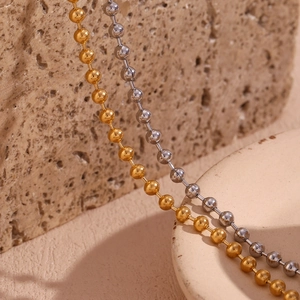 Macro shot of 4mm gold and silver stainless steel ball chains on textured stone