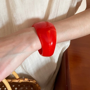 Close-up of a wide irregular red resin bangle on a wrist with warm aesthetic background