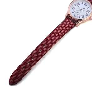 Macro detail of minimalist quartz watch featuring rose gold case and red textured strap