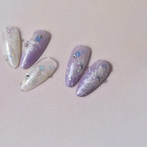 Detail of almond-shaped nails with white flowers, rhinestones and purple gradient glitter