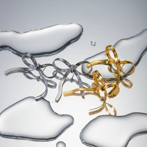 Bow stud earrings in gold and silver finish reflected on a mirrored water surface