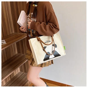 Canvas panda tote bag with brown straps shown in a cozy lifestyle setting with books