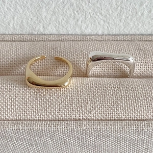 Nahaufnahme von minimalistischen Wellenringen in Gold und Silber auf strukturiertem Stoff