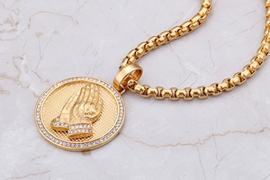 Macro detail of 18K gold plated hip-hop medallion necklace with iced-out praying hands