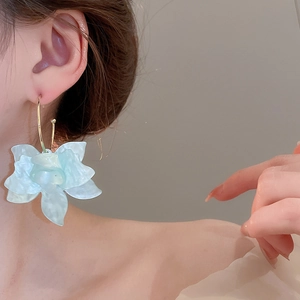 Détail de la boucle d'oreille fleur en résine bleue en forme de C sur l'oreille