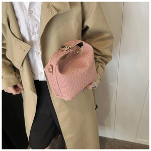 Pink woven pillow bag with gold hardware held by model in a beige trench coat