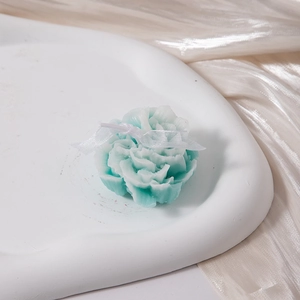 Detail of mint green carnation scented candle with ribbon on a ceramic tray