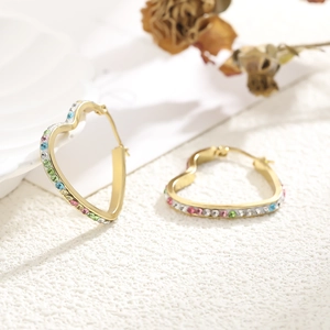 Detail of gold heart earrings with colorful crystal pavé settings on white texture