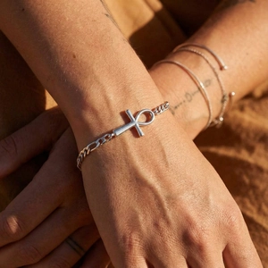 Detail showing a silver Cuban link bracelet with an Ankh cross on a person's wrist
