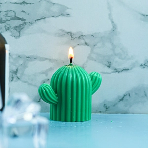 Macro detail of a green cactus-shaped candle lit with a bright steady flame on desk