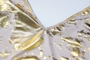 Close-up of V-neckline with shimmering gold foil leaf print on beige summer dress fabric