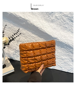 Détail d'une pochette matelassée marron montrant la texture 3D et le zip métallique