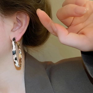 Detail of leopard print hoop earrings in metal worn by a model in a minimal setting