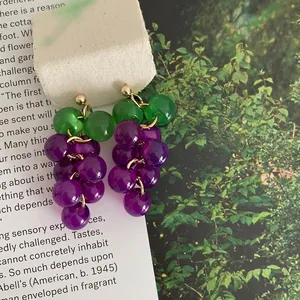 Macro view of purple resin grape earrings with green leaf details and gold-tone hooks