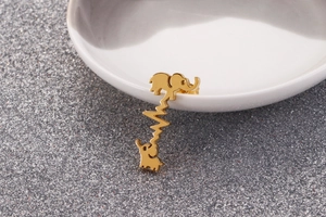 Macro shot of gold elephant and heartbeat stud earrings on white ceramic dish