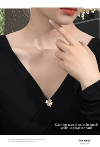 Detail of a gold-trimmed white clover brooch pinned on a black V-neck garment