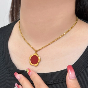 Elegant gold necklace with flower pendant featuring a red center worn by a model