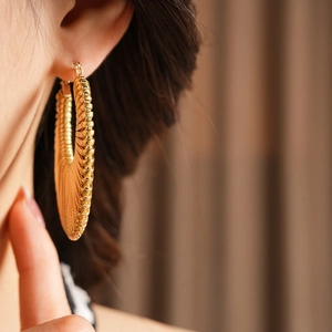Close-up of a model wearing gold textured hoop earrings with a vintage twisted design