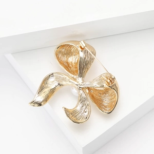 Close-up of golden bow brooch with brushed metal texture and pearl detail