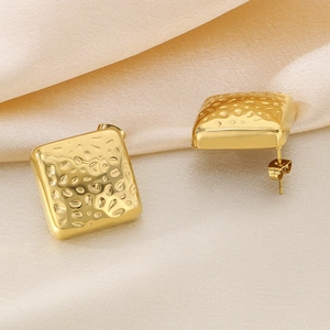 Detail von goldenen geometrischen Ohrringen mit Hammerschlag-Textur auf Champagner-Seide