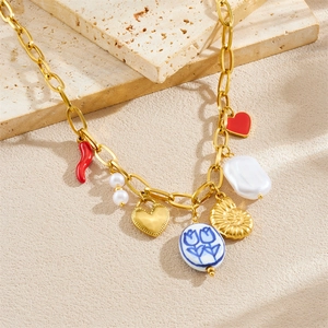 Gold charm necklace with red chili, heart lock, pearls, and sea shell on a stone background