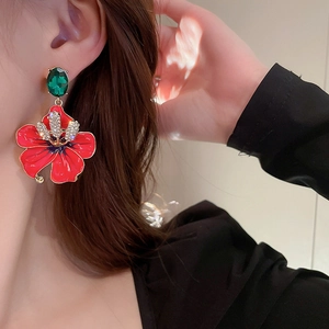 Close-up of vintage orange flower earrings with green gem worn by a model in soft light