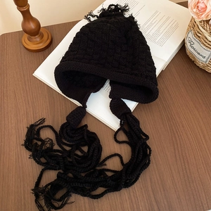 Detail of black chunky knit earflap hat with long braided tassels and soft pompom