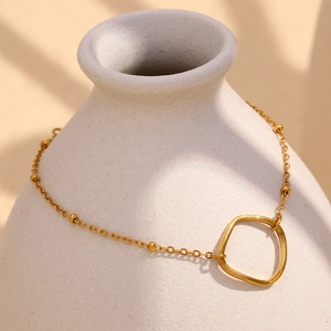 Dettaglio di bracciale in acciaio placcato oro 18K con ciondoli su un vaso bianco
