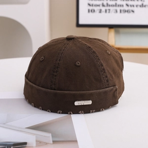 Detail of a brown cotton miki hat featuring a raw frayed edge and a silver metal tag