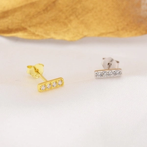 Macro shot of minimalist gold and silver stud earrings with zircons on white silk
