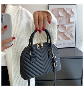Detail of black V-quilted shell bag with gold zippers and adjustable shoulder strap