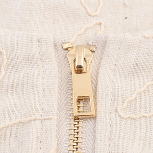 Short beige embroidery jacket with golden metal zipper detail and linen texture