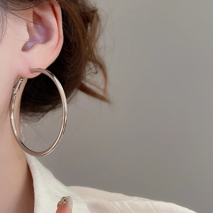 Close-up of minimalist large silver hoop earrings worn to show smooth metallic finish
