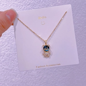 Dettaglio collana orso dorata con testa in resina blu e corpo di cristallo su carta bianca