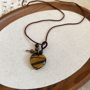Macro view of a heart-shaped tiger eye stone pendant on a brown woven cord necklace