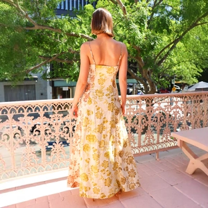 Floral backless maxi dress with spaghetti straps in yellow and white, back view on a terrace