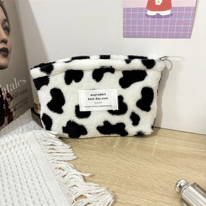 Detailed view of rectangle cow print plush makeup pouch on a minimalist wooden desk