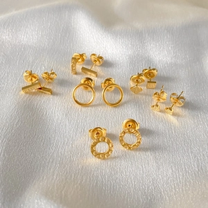 Detail of multiple gold geometric stud earrings on white silk fabric background.