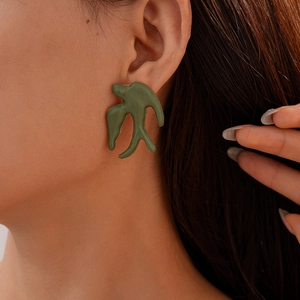 Vue latérale d'une boucle d'oreille oiseau verte avec bordure dorée sur un modèle