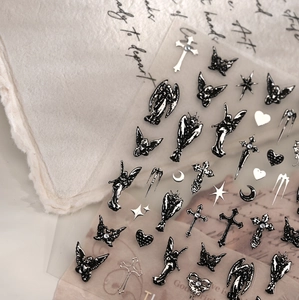 Macro shot of gothic black angel nail stickers with embossed silver cross and heart patterns