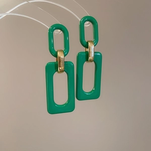Détail de boucles d'oreilles en résine verte avec maillons sur un support acrylique