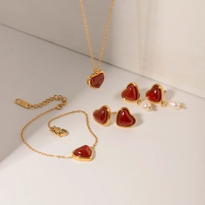 Detailed view of red heart necklace, bracelet and pearl earrings in gold plated finish