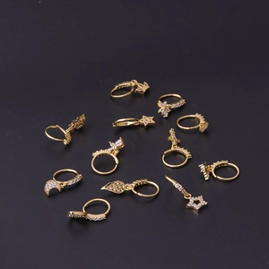 Golden 20G nose rings set with zircon star, moon and cross pendants on dark background