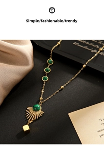 Detail of gold fan-shaped necklace with malachite stones and cube pendant on silk background