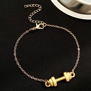 Golden dumbbell charm bracelet with O-chain and lobster clasp on black textured background