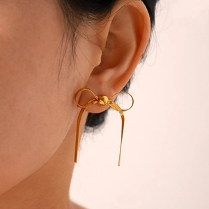 Close-up of golden ribbon bow earrings with woven metal texture worn by a model