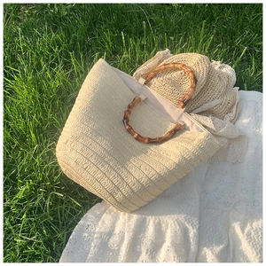 Close-up of woven straw tote bag with natural bamboo handles on white lace and green grass